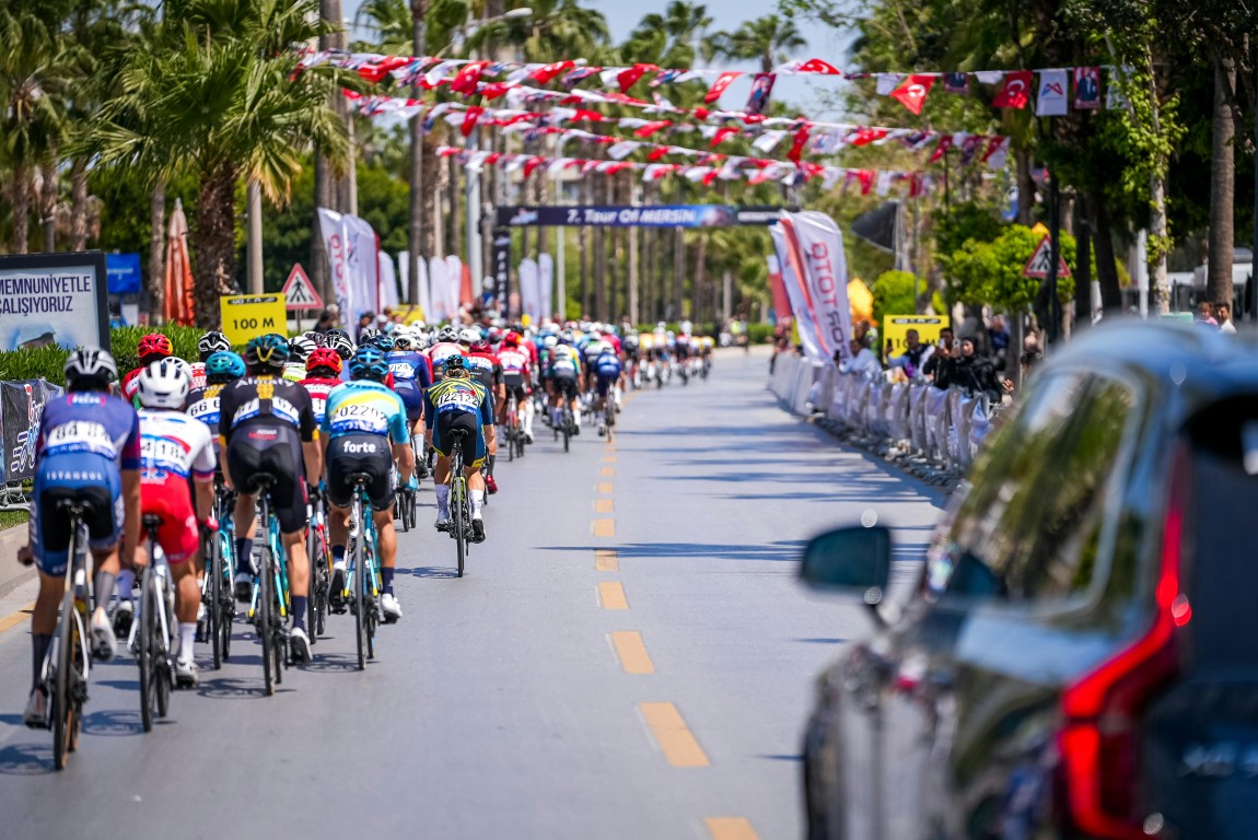 Professional cyclists racing along the Alanya coastline with Alanya Castle in the background.