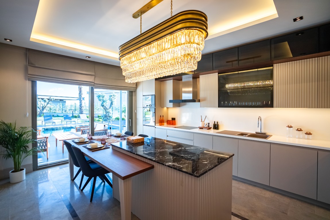 showcases a modern luxury kitchen with grey cabinets, a marble island, and sliding glass doors that open directly to the private pool area.