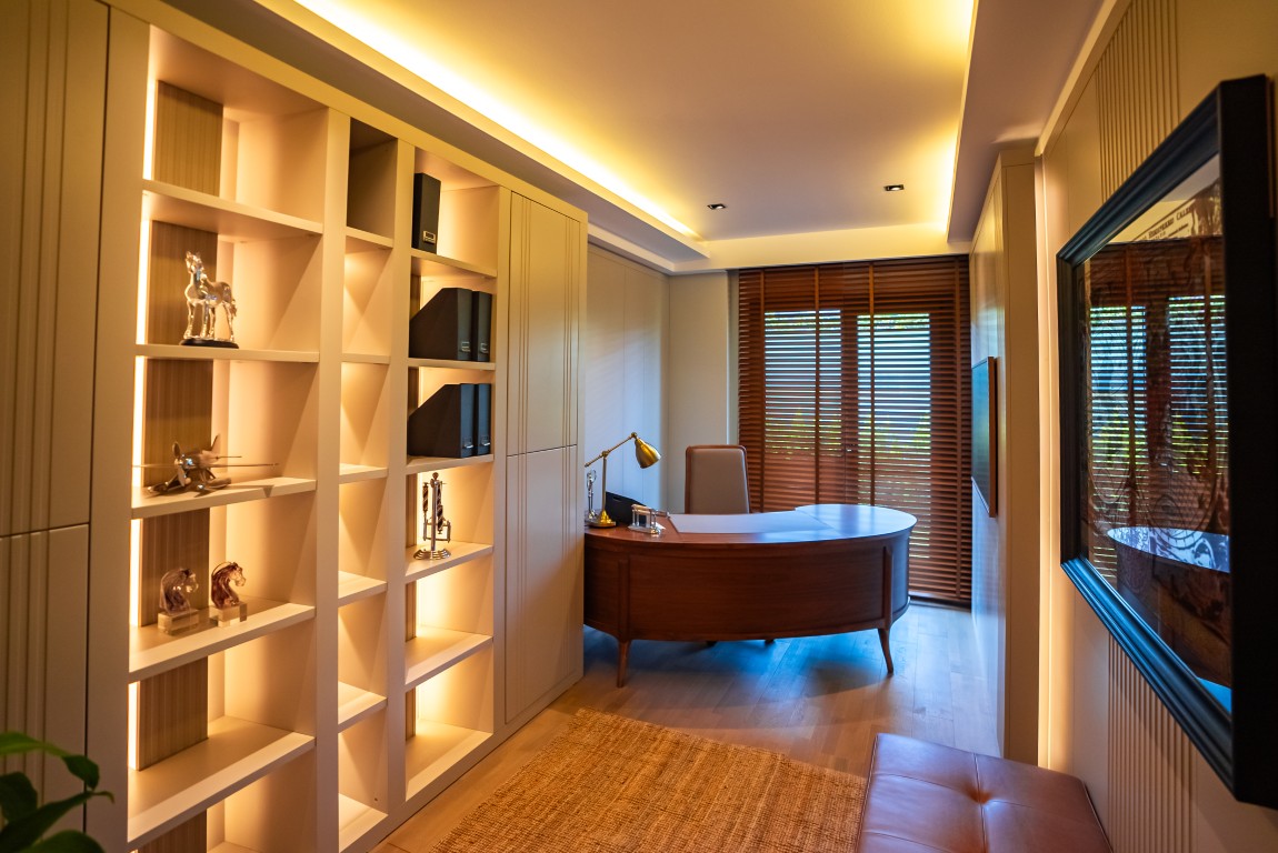 JPEG presents an elegant home office setup featuring custom wooden library shelves, a classic desk, and warm ambient lighting.