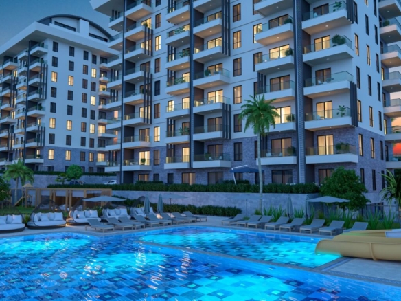 Luxury apartments for sale in Payallar showing the Konak Towers outdoor swimming pool, water slide, and modern building exterior at sunset.