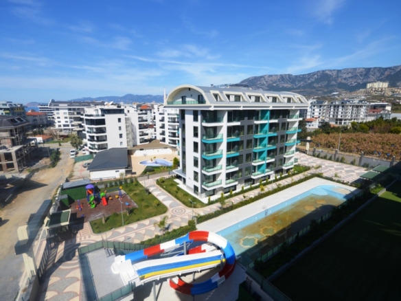 Elevated outdoor view of a luxury residential complex with water slides, a swimming pool, and a playground, as seen in the file DSC_0069 (Orta).JPG, featuring apartments for sale in Alanya.