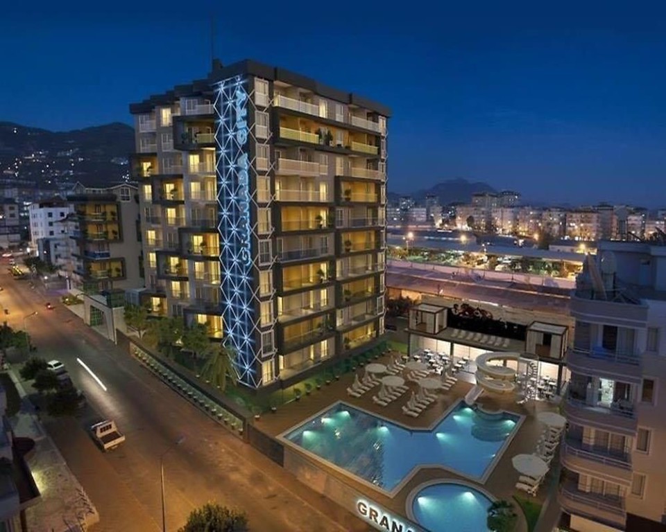 furnished 1+1 apartment for sale in Kleopatra Alanya exterior view with swimming pool and building facade at night