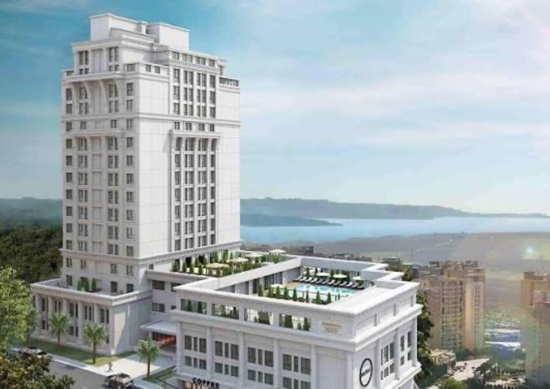 An exterior, elevated 3D architectural rendering of a multi-tiered, classical-inspired white hotel or residential complex. The complex features a high-rise tower set back on a detailed podium base. Multiple terrace levels are visible: the main terrace features a large rectangular swimming pool surrounded by dozens of white lounge chairs and tables with umbrellas; the next level down has further dining areas. Lush green landscaping, including potted plants and small trees, integrates throughout the terraces and surrounds the base of the building. The structure is built into a hillside overlooking a wide body of water (likely a large lake or bay), with a distant urban panorama across the water under a partly cloudy sky. At ground level, a street with vehicles is visible, and 'COFFEE' signage is on the building's facade. A small round 'NAP' logo is on the podium wall. The view is clear and sunny."