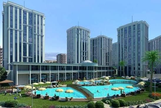 Exterior visualization of a modern residential complex and hotel, referenced by file name PHOTO-2025-10-30-15-15-59(11).jpg, featuring high-rise towers, a large swimming pool, sun umbrellas, and landscaped gardens.