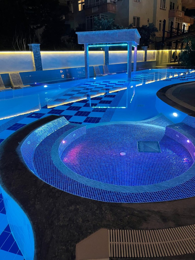Illuminated outdoor swimming pool at night in Konak Twin Tower 2 residential complex in Cleopatra Alanya
