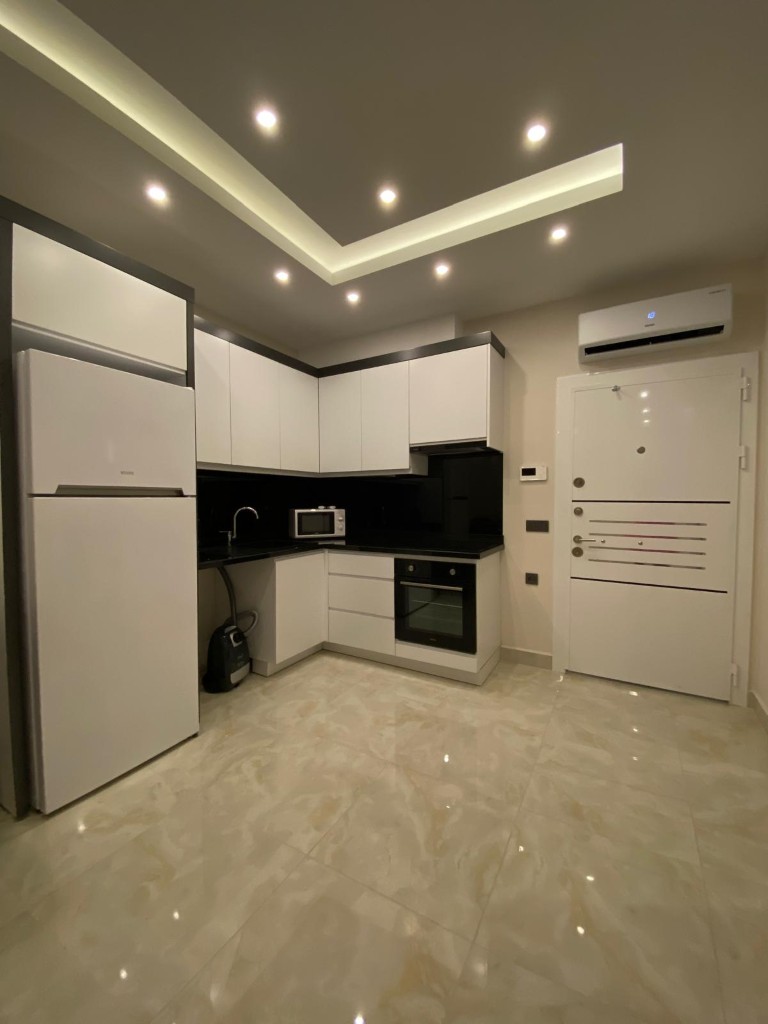 Interior view showing a modern black and white kitchen, a large white refrigerator, air conditioning unit, and a white steel entrance door