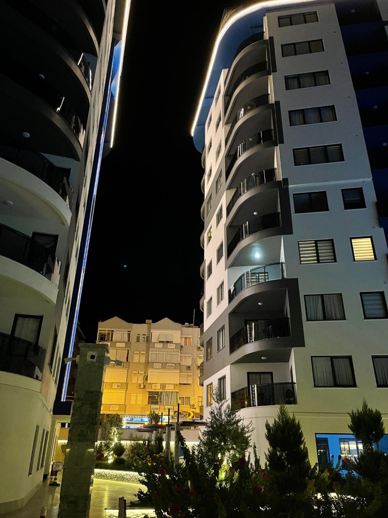 Modern high-rise residential building exterior at night showing glass balconies at Konak Twin Tower 2 in Cleopatra Alanya