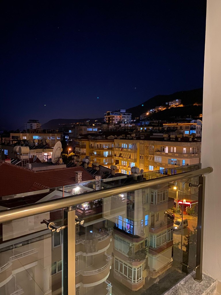 Nighttime city and mountain view from a glass-railed balcony of an apartment in Cleopatra Alanya