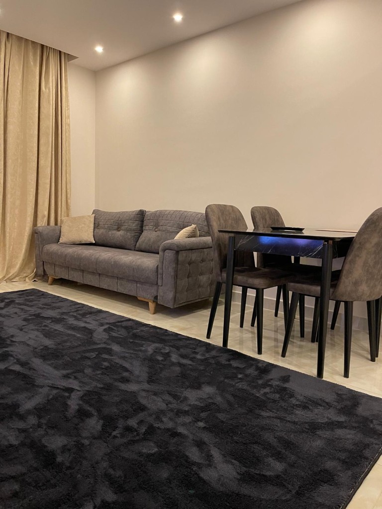 Furnished living room featuring a grey sofa, black dining table with matching chairs, and a dark rug on a light tiled floor