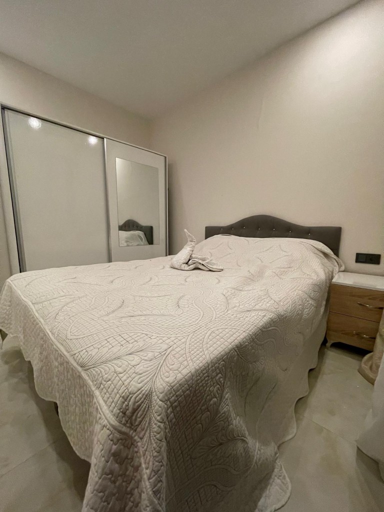 Furnished bedroom with a double bed, decorative towel art, and a white sliding door wardrobe with a mirror