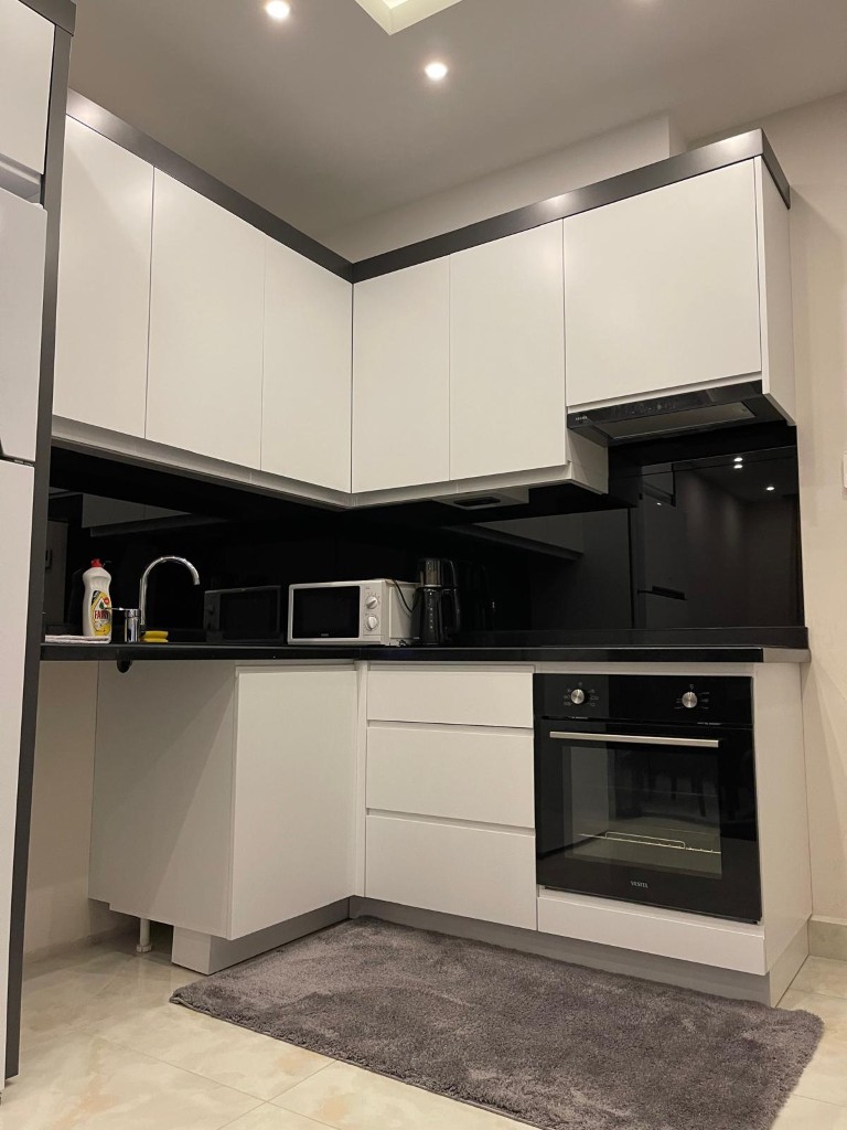Modern corner kitchen with white cabinets, black backsplash, built-in oven, microwave, and light tiled floor