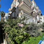 Alanya Kleopatra Plajı yakınında satılık 2 yatak odalı dairenin bulunduğu Gemicioğlu binasının yeşil ağaçlarla çevrili dış görünümü