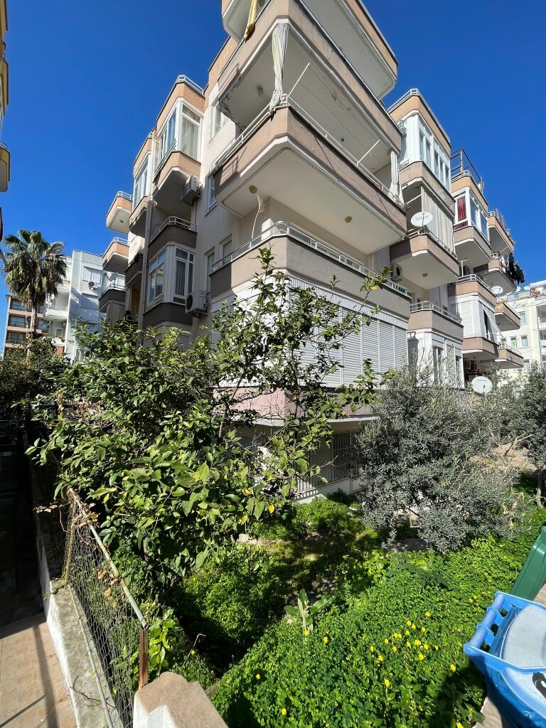 Exterior view of Gemicioglu building surrounded by green trees featuring a 2 bedroom apartment for sale near Kleopatra beach Alanya