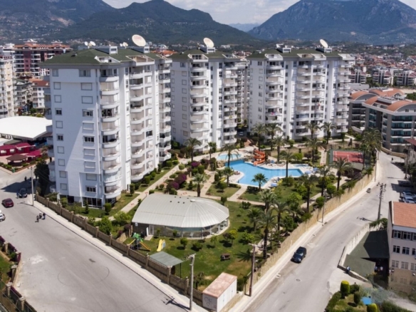Högt perspektiv över Galaxy-komplexet med utomhuspool och tennisbana, som erbjuder en lägenhet med 2 sovrum till salu i Cikcilli, Alanya