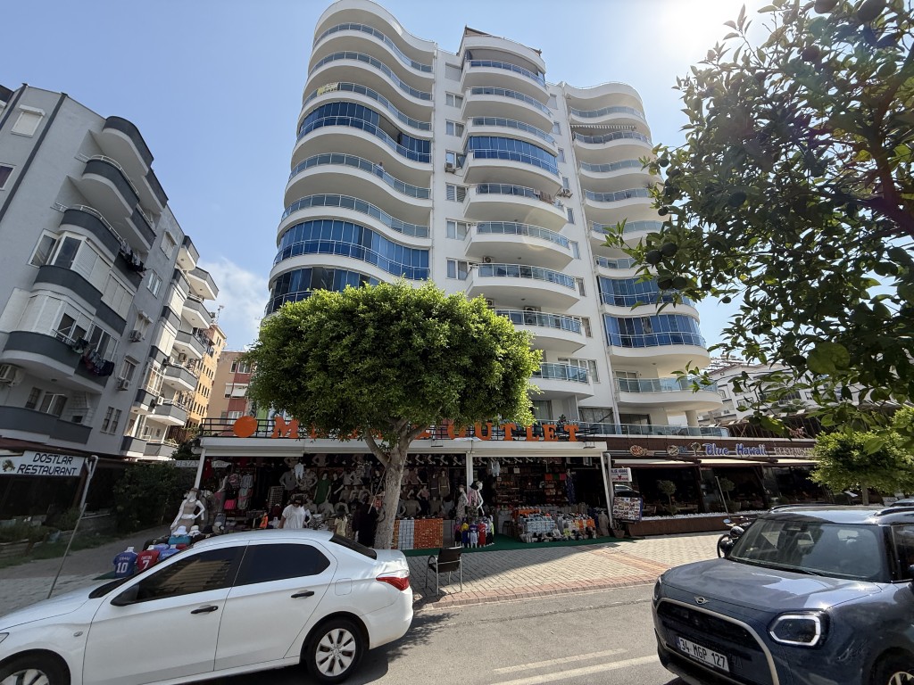 Exterior front view of Beyaz Apartmanı multi-story residential building in Mahmutlar Alanya featuring ground floor shops and curved glass balconies