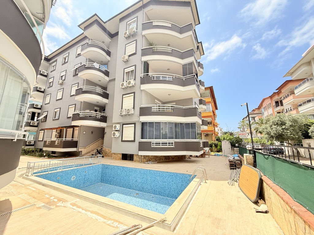 Exterior view of Ergün Bey residential building in Oba Alanya featuring a courtyard outdoor swimming pool and private balconies