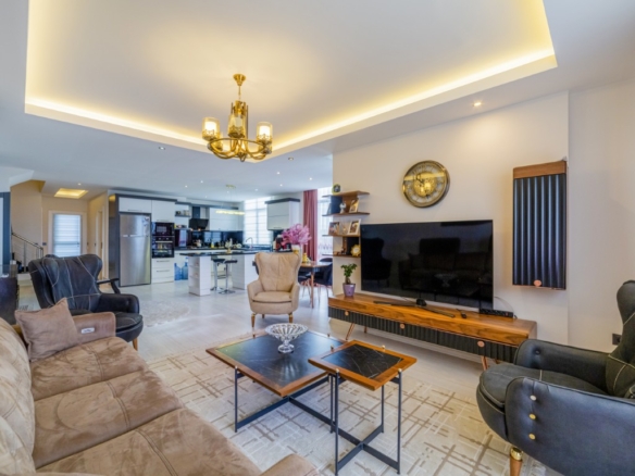 Spacious and modern living room of the penthouse in Tosmur Alanya featuring comfortable seating, a flat-screen TV, and an open-plan kitchen in the background.
