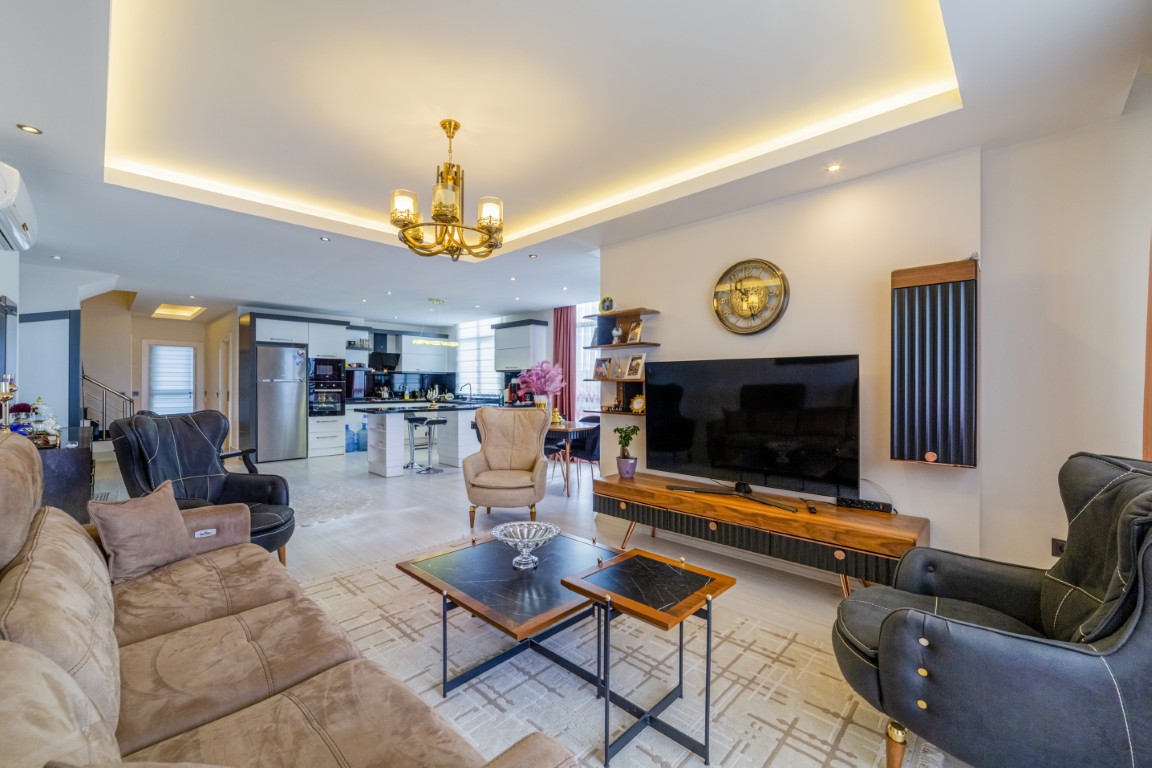 Spacious and modern living room of the penthouse in Tosmur Alanya featuring comfortable seating, a flat-screen TV, and an open-plan kitchen in the background.